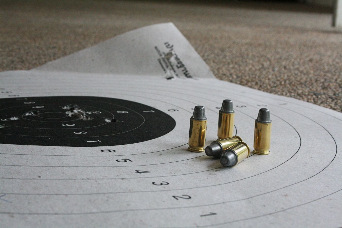 Stock photo, illustrative. A paper target with holes, and several cartridges lying on the target.